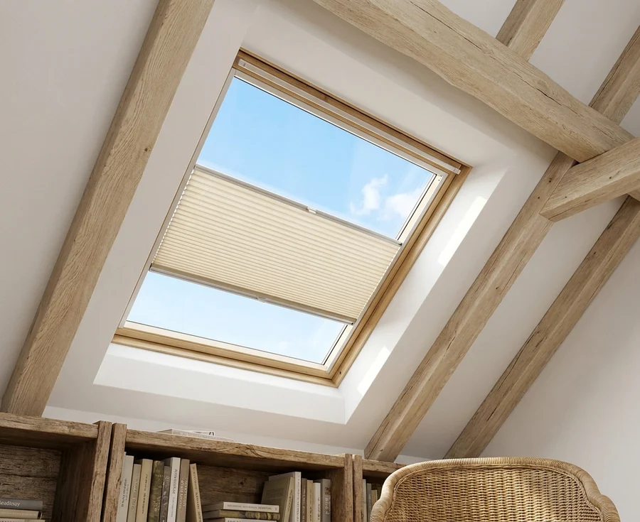 Pleated skylight blind pulled part-way across a roof window set between heavy oak rafters in the upstairs reading nook of a Cornwall Hill house, blue sky showing above and below it
